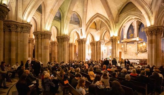 La cripta de la Basílica de la Sagrada Familia, fotografiada desde la zona de entrada, con todos los asientos llenos, poco antes de que comience el concierto