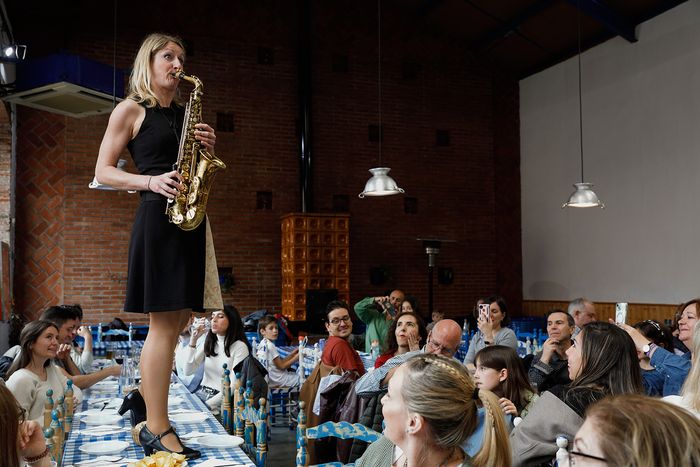 Una de las músicas de pie sobre una mesa mientras toca el saxofón, rodeada de espectadores entusiastas.