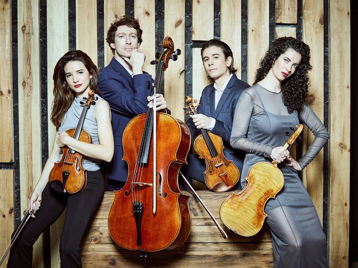 Cuatro miembros del Parallel Quartet posan con sus instrumentos de cuerda ante un fondo de madera: Alfredo Ancillo y Laura V. Hidalgo con violines, Fátima Poblete con viola y Stamen Nikolov con cello.